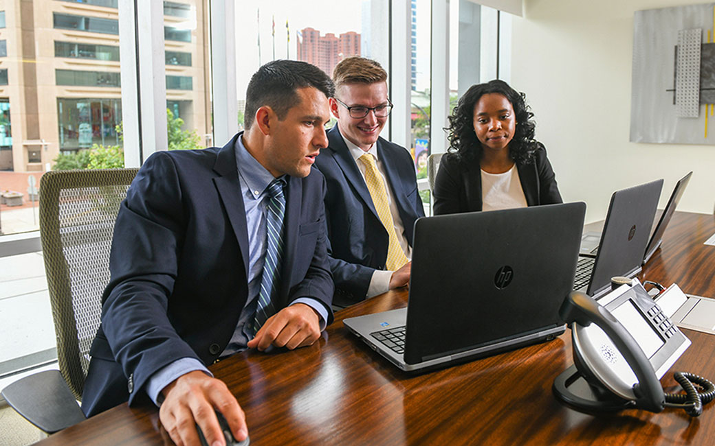 three student accounting interns working at a computer in a conference room in downtown Baltimore