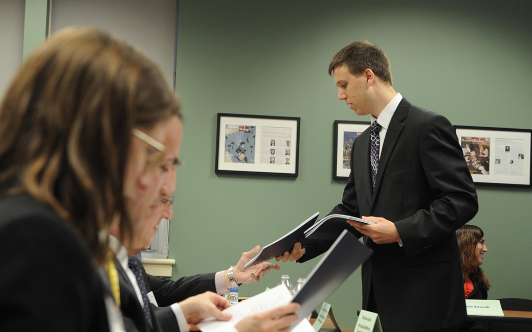 student passing out materials to a panel of judges