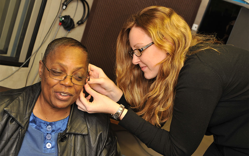 Audiology faculty fits a hearing aid on a person in a lab