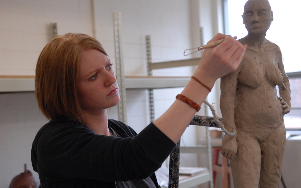 student (female) sculpting female form in clay