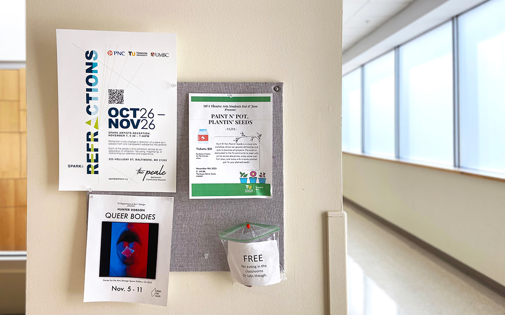 A gray cork bord full of fliers is hung up in a brightly lit hallway