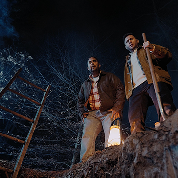 Two actors look down inside the grave they've just dug
