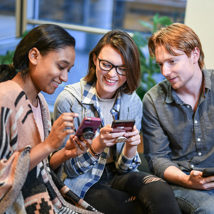 Three TU students smiling with their smartphones