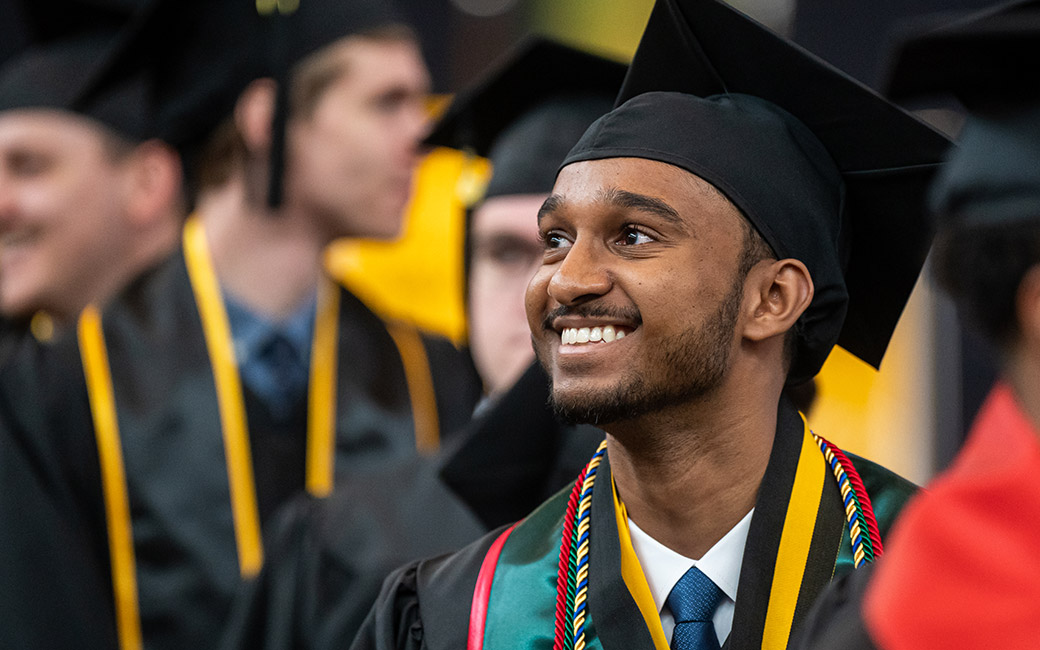 Student in commencement regalia smiling while delivering speech from stage