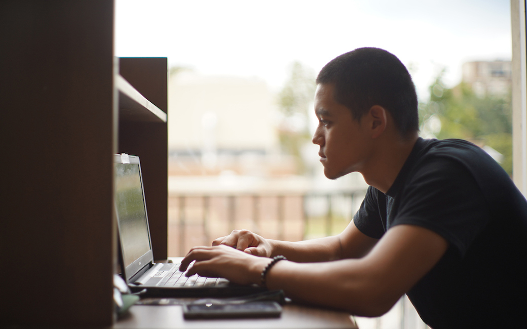 Student working on laptop in library, partially in shadow