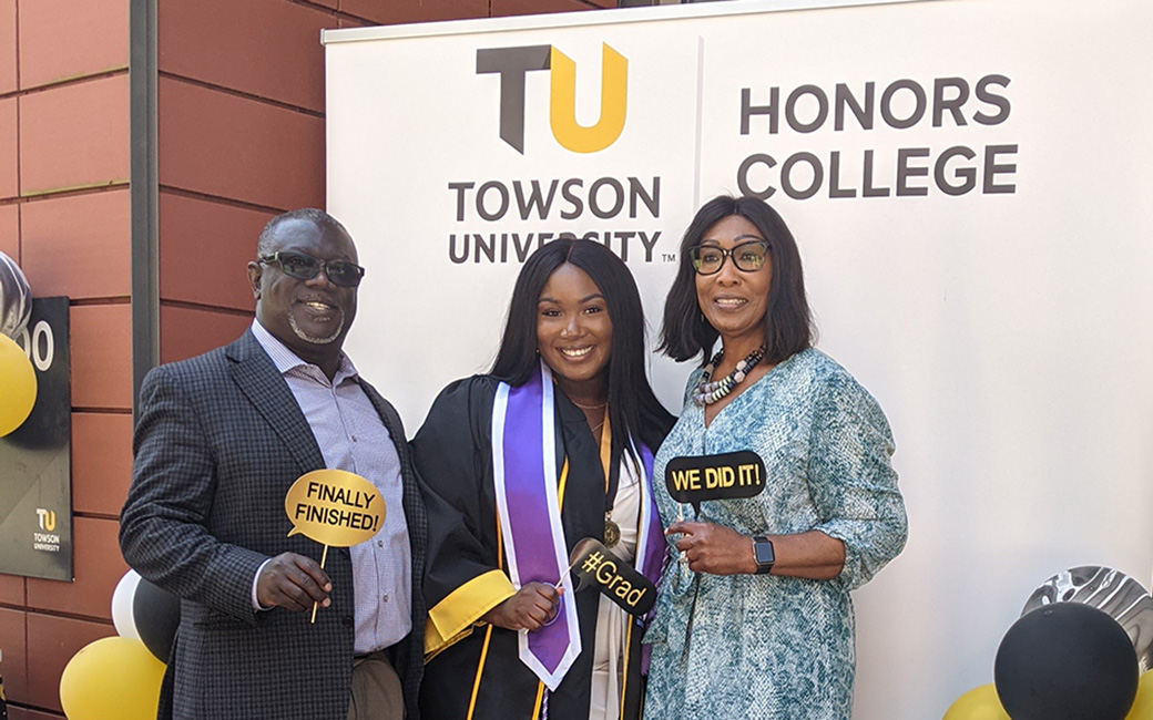 Student holding Honors certificate, flanked by parents