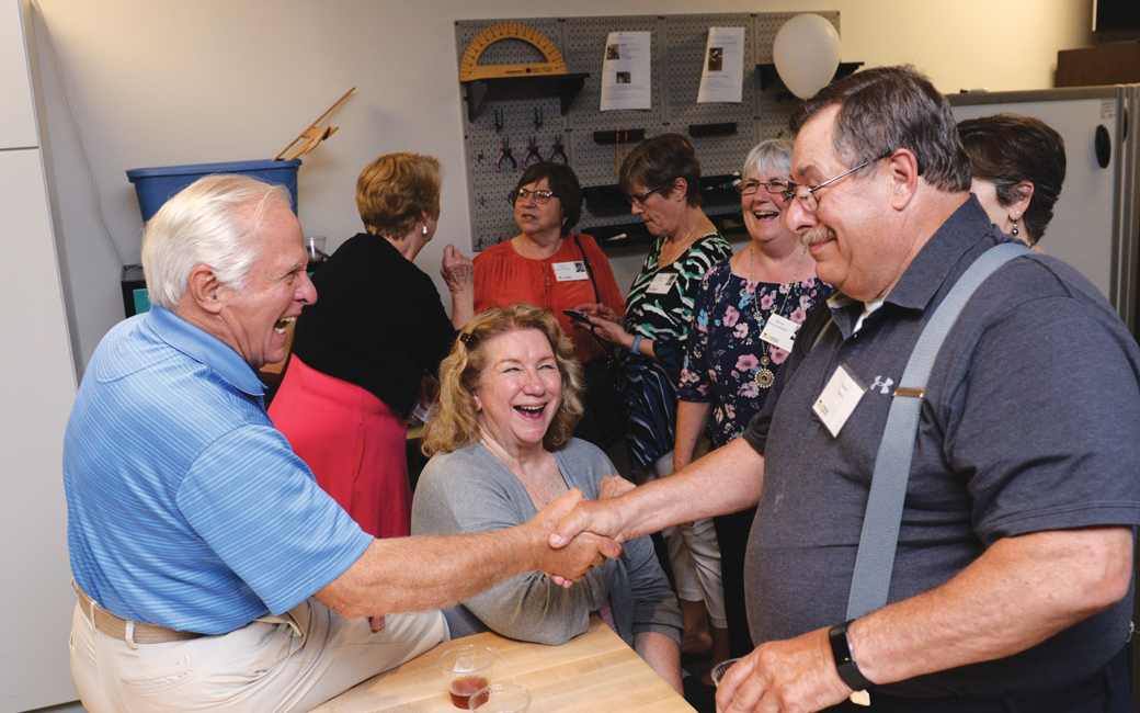 Two Class of 1969 members shake hands and laugh