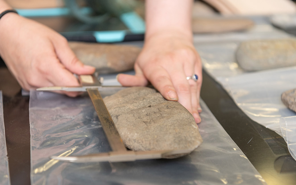 Close-up of hands measuring large stone artifact