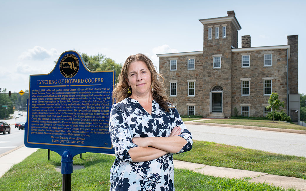 Woman stands in front of lynching memorial sign and former Baltimore County jail