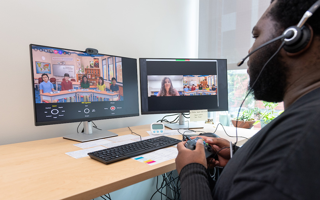 person wearing headset and holding controller in front of two monitors