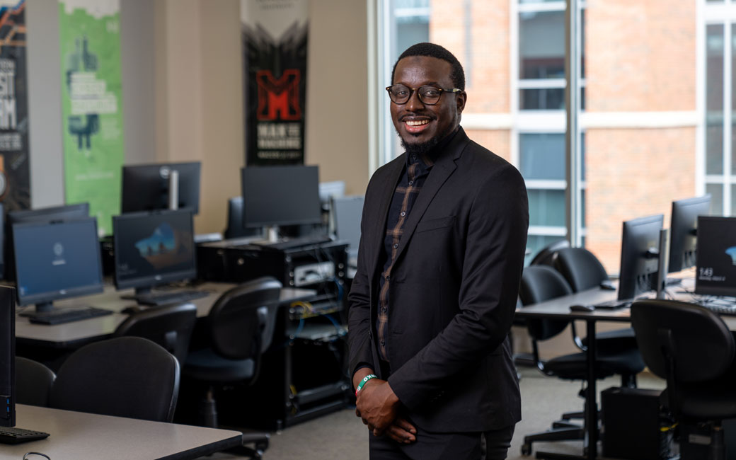 Information Technology Ph.D. candidate stands in computer lab on campus