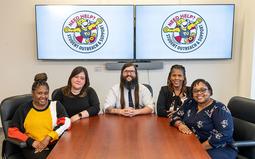 Five peopel sitting around a conference table with the SOS logo in th back