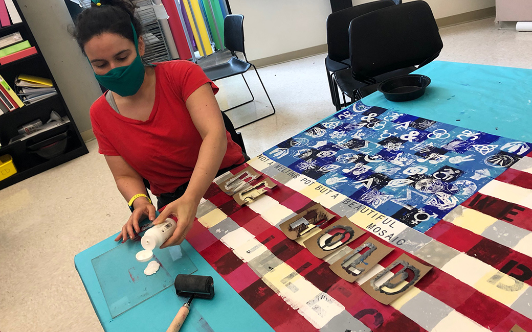 Woman wearing mask sitting at table working on flag art project