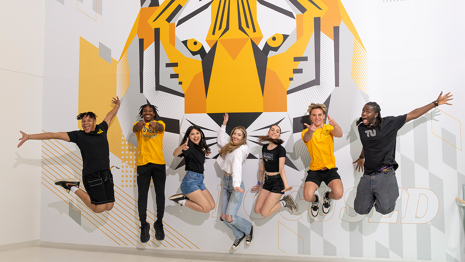 Students jumping in front of a tiger mural