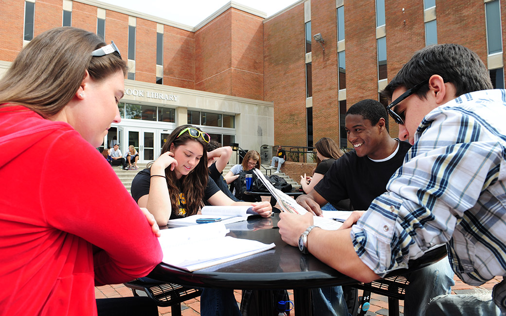 Students sit at a table reading a newspaper.