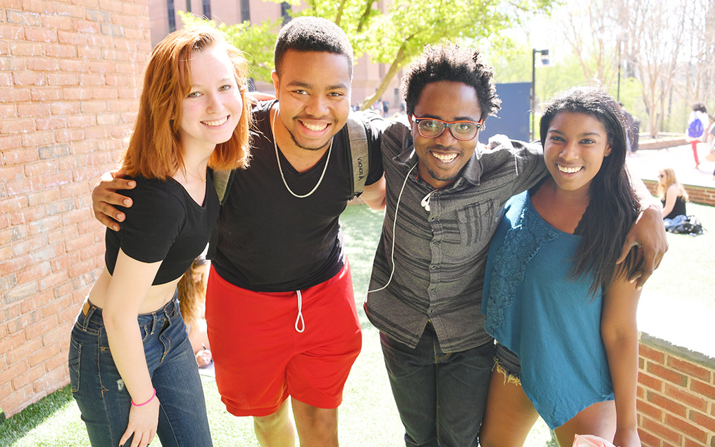 A group of four students standing and hugging together in front of Towson's freedom square